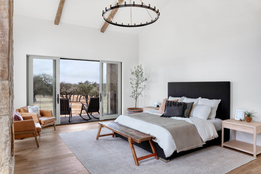 Landhausstil Hauptschlafzimmer mit weißer Wandfarbe, hellem Holzboden, Kamin, Kaminumrandung aus Stein und freigelegten Dachbalken in Austin