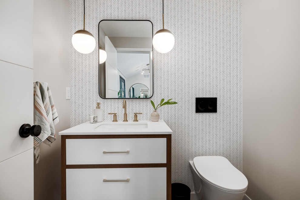 Design ideas for a small retro cloakroom in Minneapolis with flat-panel cabinets, medium wood cabinets, a wall mounted toilet, white walls, light hardwood flooring, a submerged sink, engineered stone worktops, beige floors, white worktops, a freestanding vanity unit and wallpapered walls.