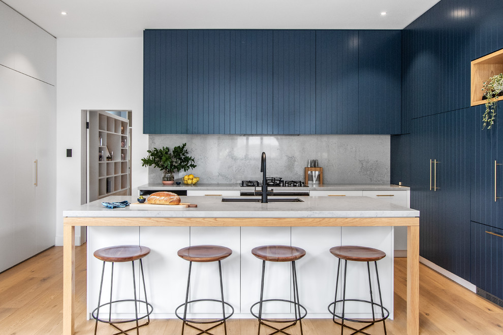 This is an example of a contemporary galley kitchen in Sydney with an undermount sink, blue cabinets, with island, grey benchtop, marble benchtops, multi-coloured splashback, marble splashback, black appliances and light hardwood floors.