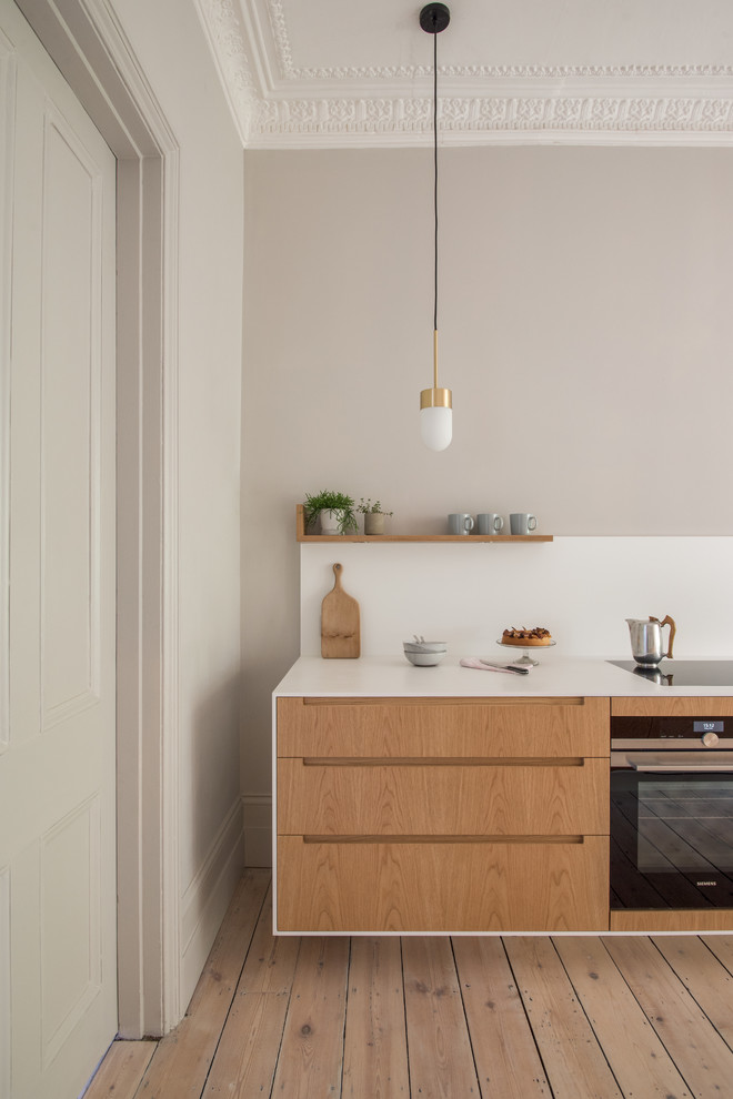 This is an example of a mid-sized modern galley eat-in kitchen in London with white splashback, light hardwood floors, an undermount sink, flat-panel cabinets, light wood cabinets, quartzite benchtops, panelled appliances and brown floor.