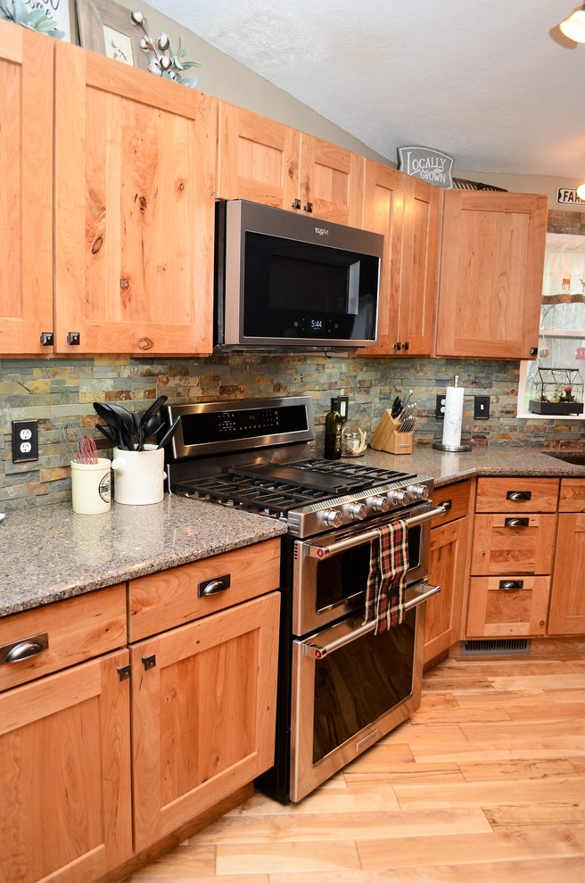 Photo of a mid-sized country galley eat-in kitchen in Other with an undermount sink, shaker cabinets, light wood cabinets, quartzite benchtops, grey splashback, stone tile splashback, stainless steel appliances, light hardwood floors, no island, brown floor and grey benchtop.
