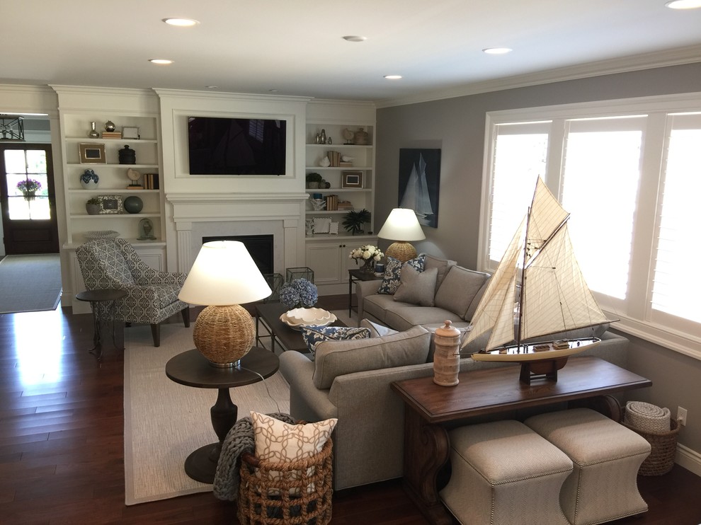 This is an example of a large beach style open concept family room in Detroit with grey walls, dark hardwood floors, a standard fireplace, a stone fireplace surround, a wall-mounted tv and brown floor.