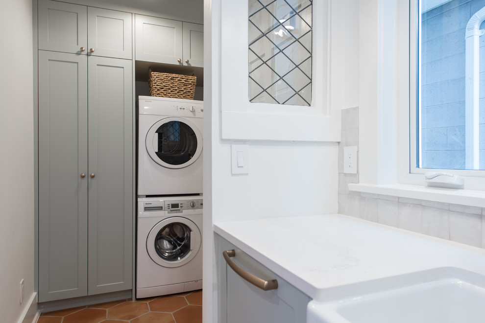 Photo of a small country single-wall utility room in Vancouver with shaker cabinets, green cabinets, white walls, terra-cotta floors, a stacked washer and dryer and orange floor.