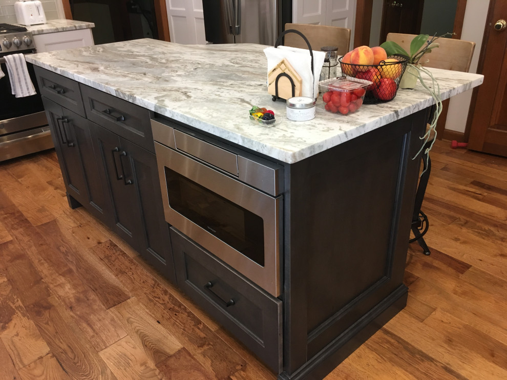 Mid-sized transitional u-shaped medium tone wood floor and brown floor eat-in kitchen photo with a farmhouse sink, recessed-panel cabinets, white cabinets, granite countertops, gray backsplash, glass tile backsplash, stainless steel appliances, an island and gray countertops