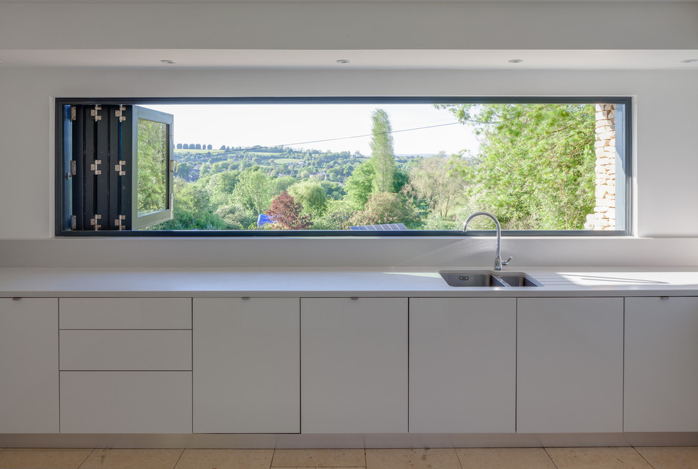 Contemporary single-wall open plan kitchen in Gloucestershire with a drop-in sink, white cabinets, white splashback, panelled appliances and with island.