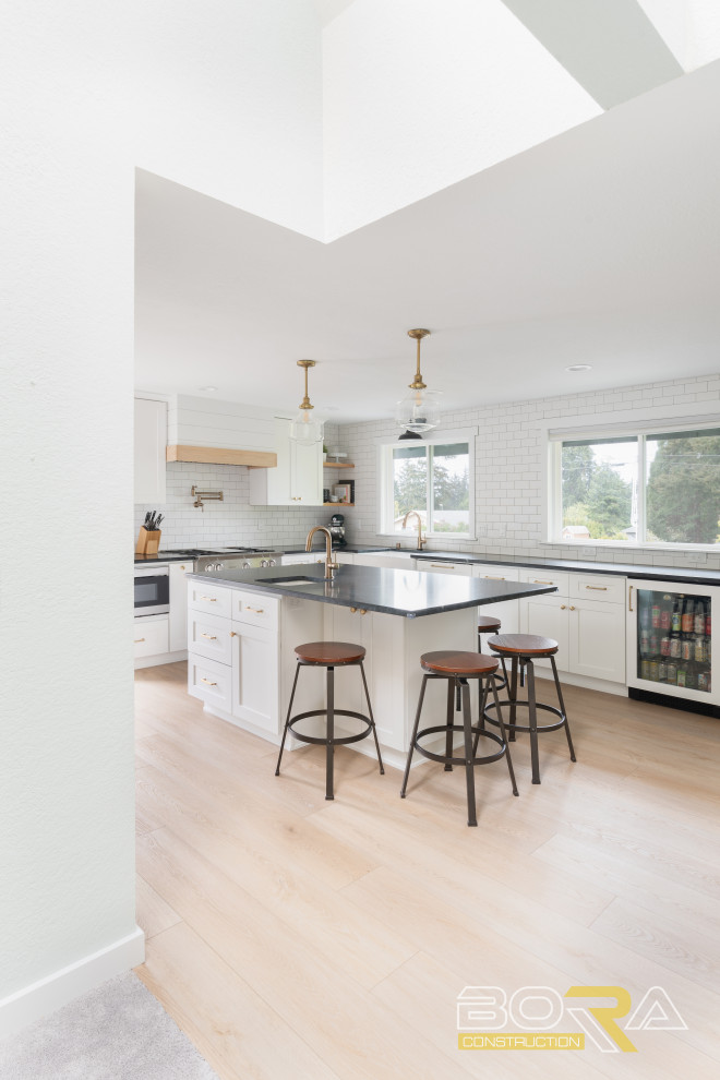 Example of a mid-sized transitional u-shaped medium tone wood floor and brown floor eat-in kitchen design in Seattle with shaker cabinets, white cabinets, quartz countertops, white backsplash, ceramic backsplash, stainless steel appliances, an island and black countertops