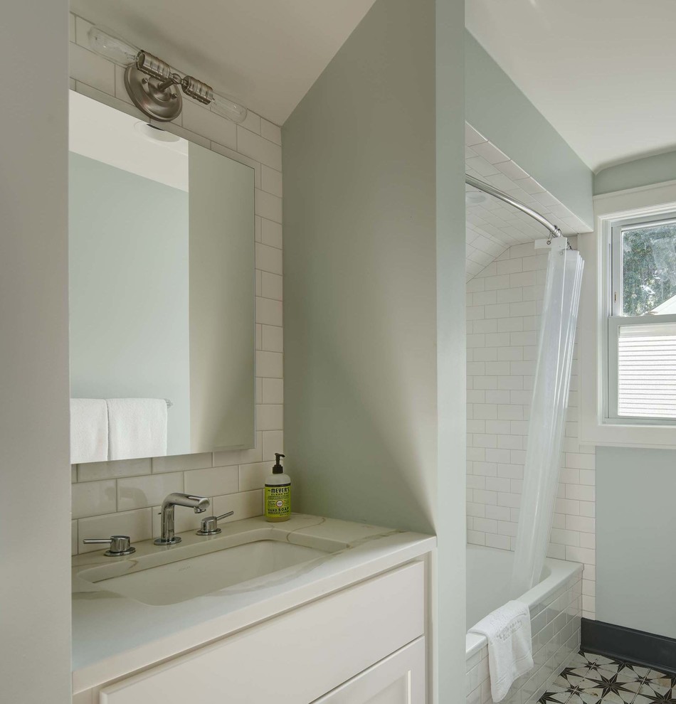 Photo of a small transitional bathroom in New York with shaker cabinets, white cabinets, a shower/bathtub combo, a two-piece toilet, white tile, ceramic tile, blue walls, porcelain floors, an undermount sink, engineered quartz benchtops, multi-coloured floor and white benchtops.