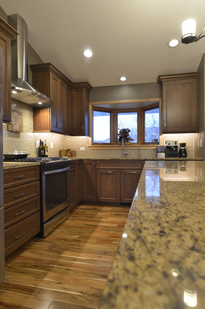 Mid-sized transitional l-shaped medium tone wood floor open concept kitchen photo in Minneapolis with a single-bowl sink, flat-panel cabinets, brown cabinets, granite countertops, beige backsplash, glass tile backsplash, stainless steel appliances and an island