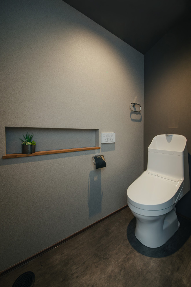 На фото: туалет в современном стиле с унитазом-моноблоком, серыми стенами, черным полом, потолком с обоями и обоями на стенах