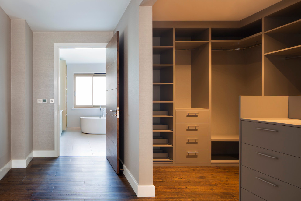 This is an example of a large modern gender-neutral dressing room in Buckinghamshire with open cabinets, grey cabinets and dark hardwood floors.