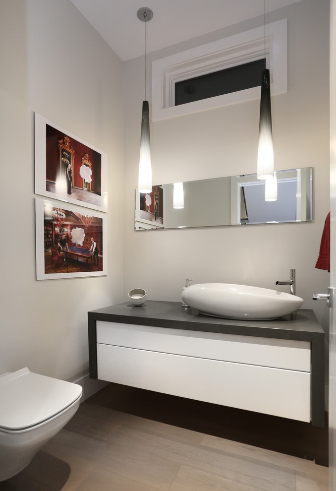 Photo of an expansive contemporary powder room in Vancouver with flat-panel cabinets, white cabinets, a wall-mount toilet, beige tile, grey walls, light hardwood floors and a vessel sink.