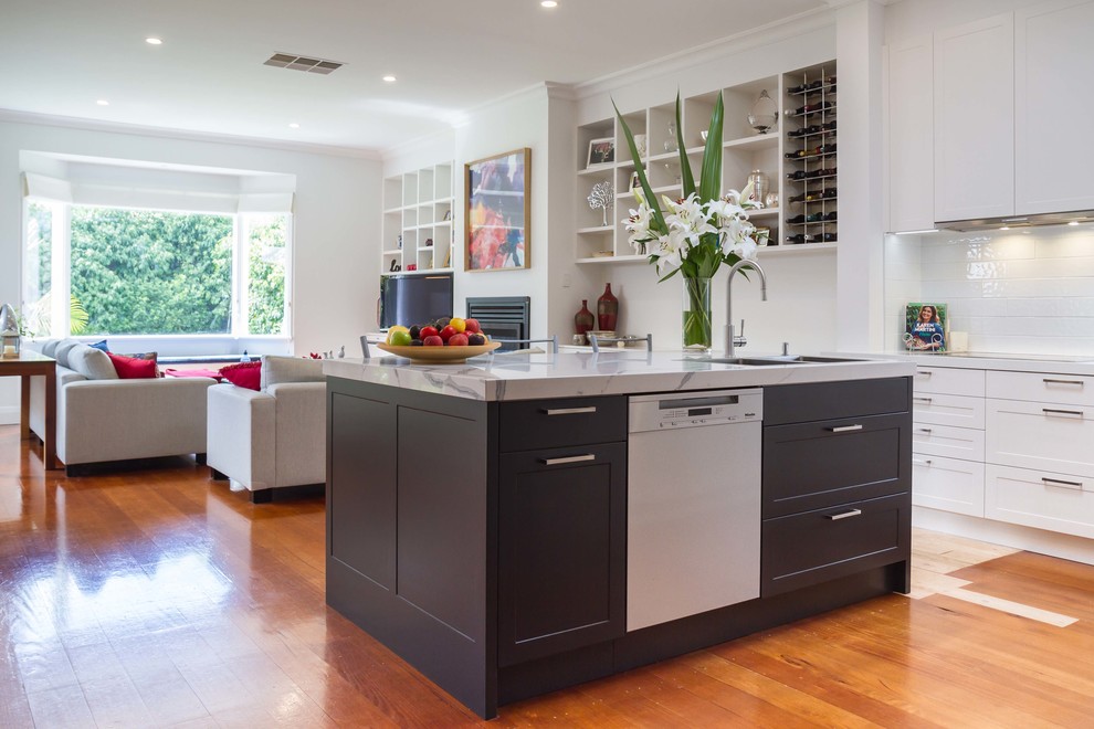 Photo of a mid-sized traditional l-shaped open plan kitchen in Melbourne with a drop-in sink, shaker cabinets, white cabinets, quartz benchtops, white splashback, porcelain splashback, medium hardwood floors and with island.