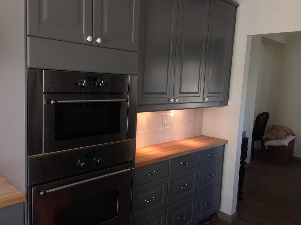 Enclosed kitchen - transitional laminate floor and brown floor enclosed kitchen idea with a farmhouse sink, shaker cabinets, blue cabinets, wood countertops, white backsplash, subway tile backsplash and stainless steel appliances