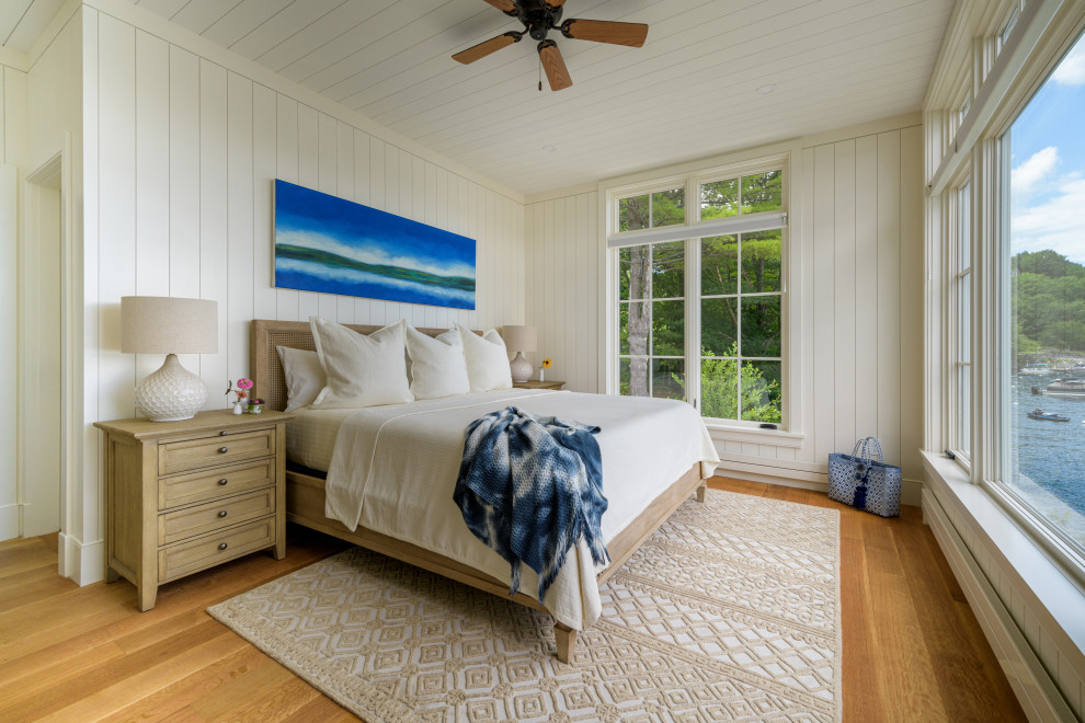 Diseño de dormitorio principal marinero con paredes blancas, suelo de madera en tonos medios, suelo marrón y panelado