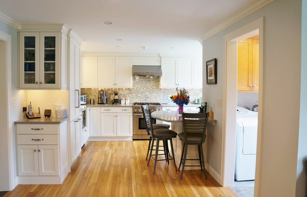 Eat-in kitchen - mid-sized transitional l-shaped light wood floor eat-in kitchen idea in Boston with a farmhouse sink, shaker cabinets, white cabinets, quartz countertops, blue backsplash, glass tile backsplash, paneled appliances and a peninsula