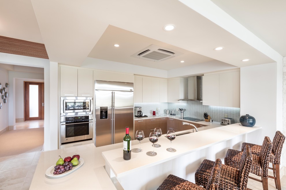 Photo of a mid-sized transitional u-shaped kitchen in Other with an undermount sink, flat-panel cabinets, beige cabinets, quartz benchtops, blue splashback, glass tile splashback, stainless steel appliances, travertine floors and a peninsula.