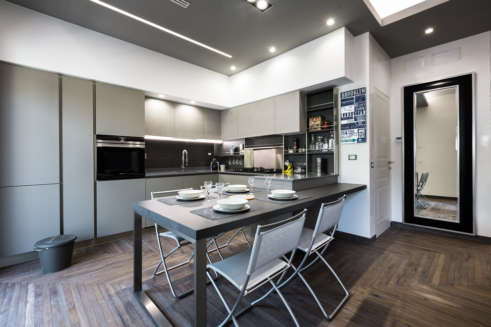 Photo of a contemporary l-shaped eat-in kitchen in Rome with flat-panel cabinets, grey cabinets, black splashback, black appliances, dark hardwood floors, black benchtop, an undermount sink, a peninsula and brown floor.