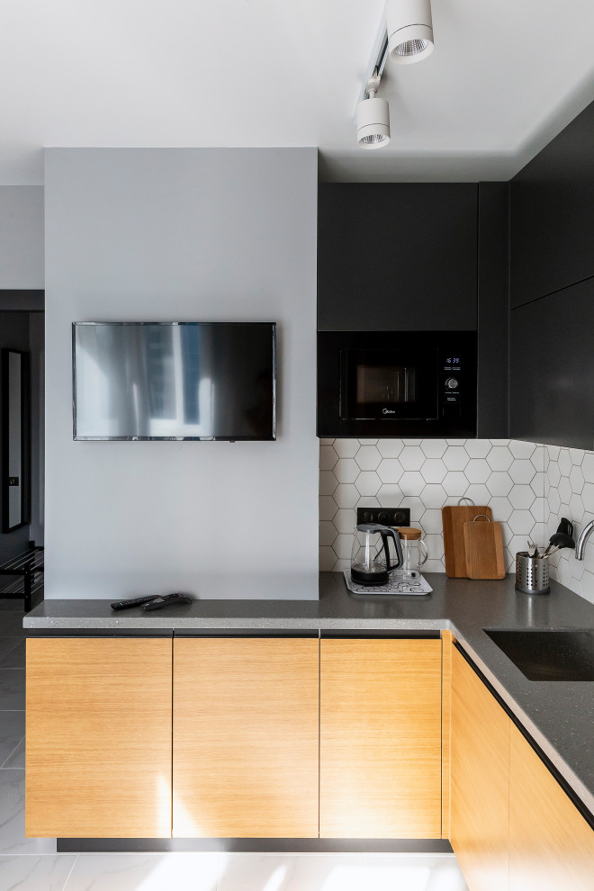 Mid-sized contemporary l-shaped kitchen in Moscow with an undermount sink, flat-panel cabinets, light wood cabinets, white splashback, porcelain splashback, black appliances, porcelain floors, grey floor and grey benchtop.