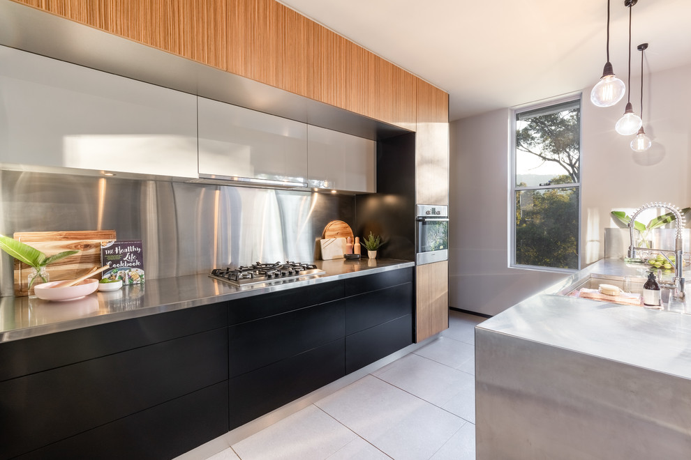 Photo of a modern kitchen in Other with an integrated sink, flat-panel cabinets, black cabinets, stainless steel benchtops, metallic splashback, no island, white floor and grey benchtop.