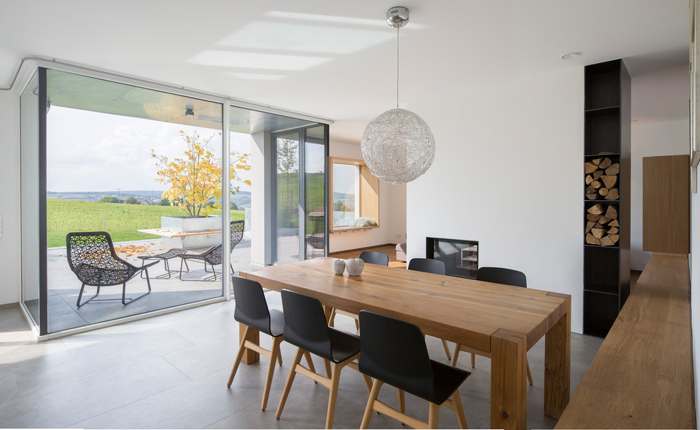 This is an example of a mid-sized contemporary open plan dining in Other with white walls, concrete floors, a two-sided fireplace, a plaster fireplace surround and grey floor.