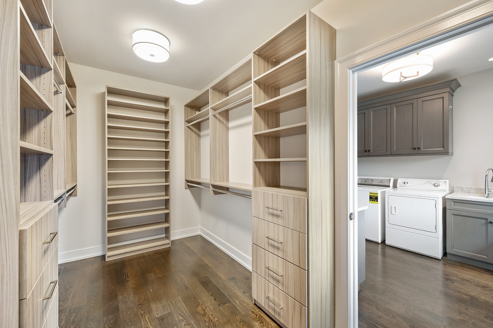 This is an example of a mid-sized transitional gender-neutral dressing room in Chicago with flat-panel cabinets, light wood cabinets, dark hardwood floors and brown floor.