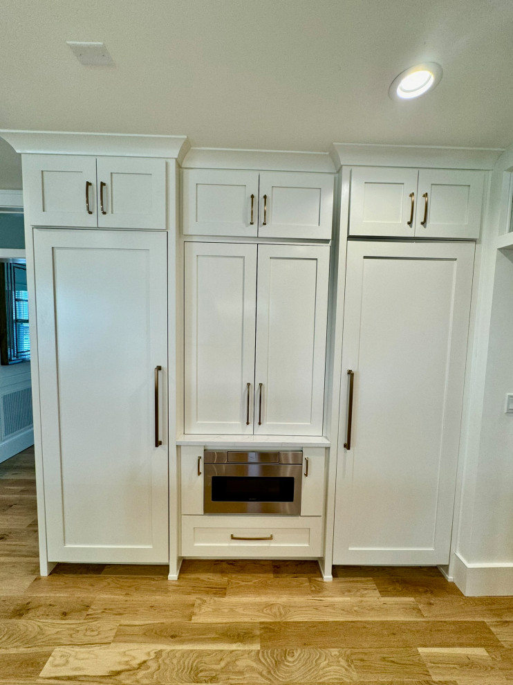 Example of a mid-sized transitional l-shaped light wood floor, brown floor and wallpaper ceiling eat-in kitchen design in Atlanta with a farmhouse sink, shaker cabinets, white cabinets, granite countertops, white backsplash, stainless steel appliances, an island and white countertops