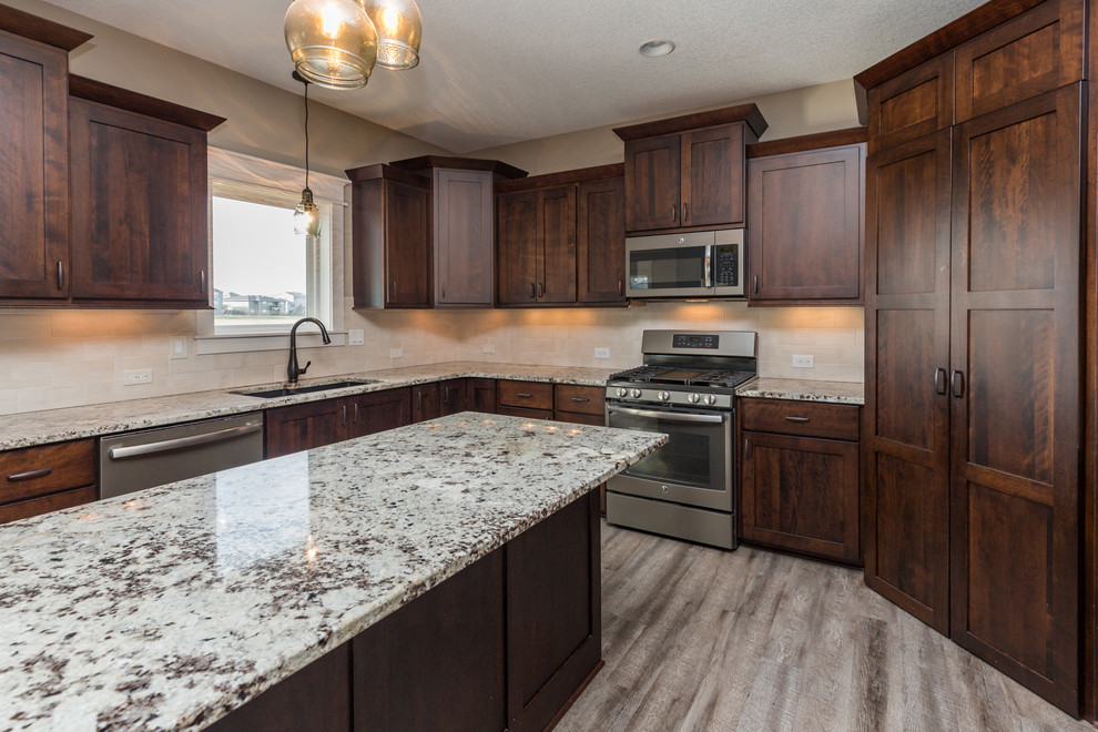 Example of a transitional u-shaped vinyl floor and gray floor eat-in kitchen design with an undermount sink, shaker cabinets, dark wood cabinets, granite countertops, beige backsplash, ceramic backsplash, stainless steel appliances, an island and beige countertops