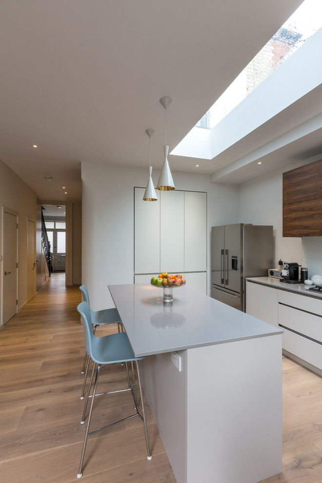 Design ideas for a mid-sized contemporary l-shaped open plan kitchen in London with flat-panel cabinets, white cabinets, quartzite benchtops, white splashback, glass sheet splashback, light hardwood floors, with island, beige floor and white benchtop.