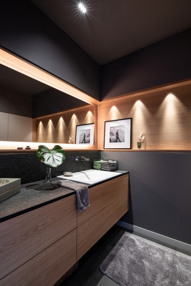 This is an example of a large contemporary 3/4 bathroom in Other with black walls, ceramic floors, a drop-in sink, granite benchtops, grey floor, a floating vanity, wood walls, flat-panel cabinets, medium wood cabinets and black benchtops.