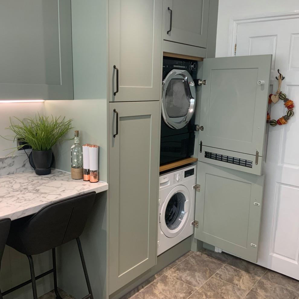 Mid-sized contemporary u-shaped laundry room in Buckinghamshire with shaker cabinets, green cabinets, laminate benchtops, white splashback, glass sheet splashback, grey floor and white benchtop.