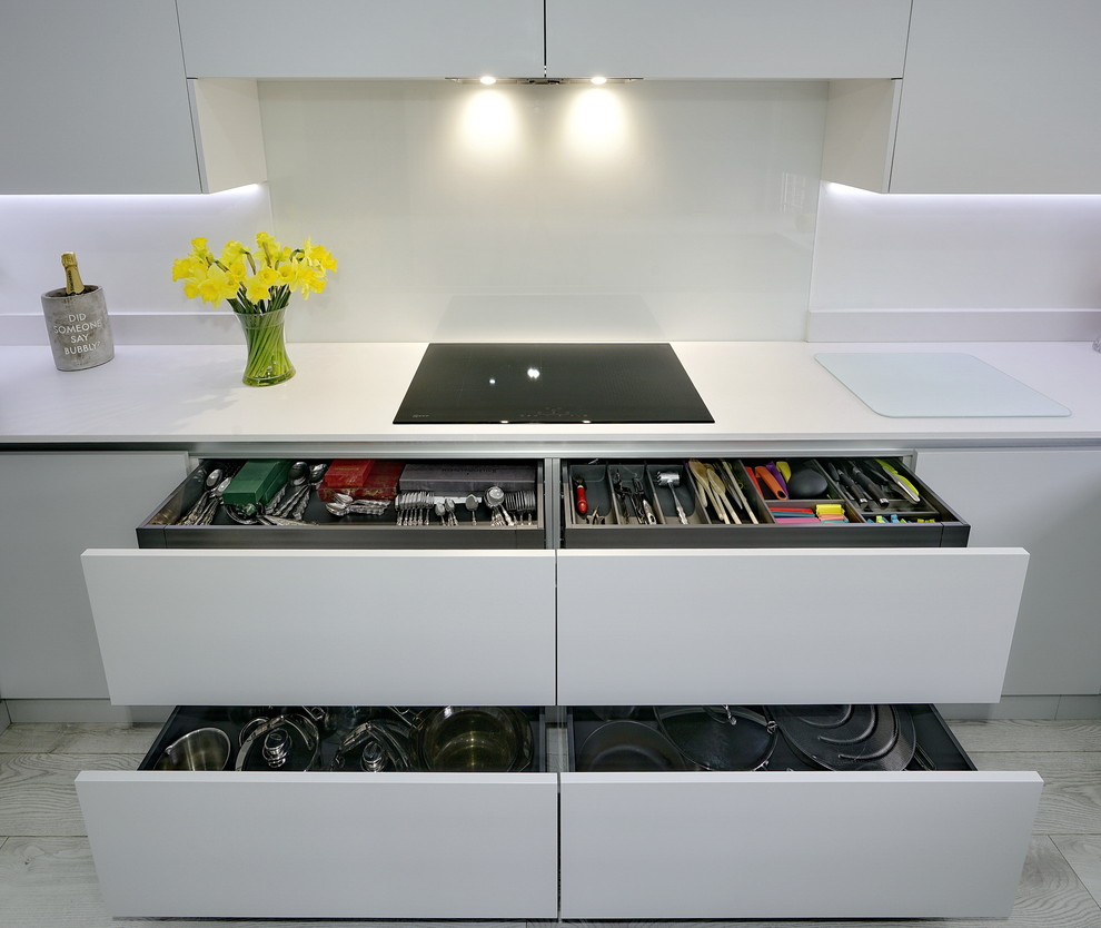 Medium sized modern u-shaped enclosed kitchen with a built-in sink, flat-panel cabinets, grey cabinets, quartz worktops, white splashback, glass sheet splashback, black appliances, laminate floors, a breakfast bar, grey floors and white worktops.