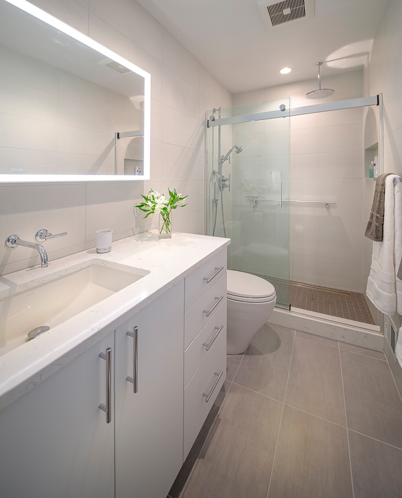 Photo of a mid-sized contemporary 3/4 bathroom in DC Metro with flat-panel cabinets, white cabinets, an alcove shower, a one-piece toilet, beige tile, porcelain tile, beige walls, laminate floors, an undermount sink, quartzite benchtops, beige floor, a sliding shower screen and white benchtops.