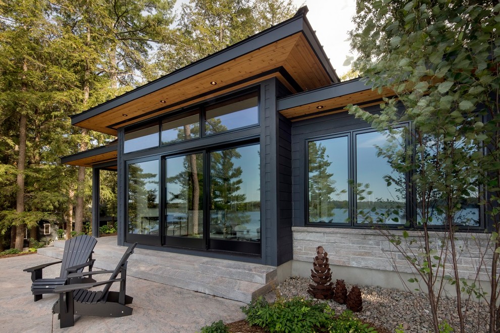 Mid-sized contemporary one-storey black house exterior in Toronto with mixed siding, a flat roof and a shingle roof.