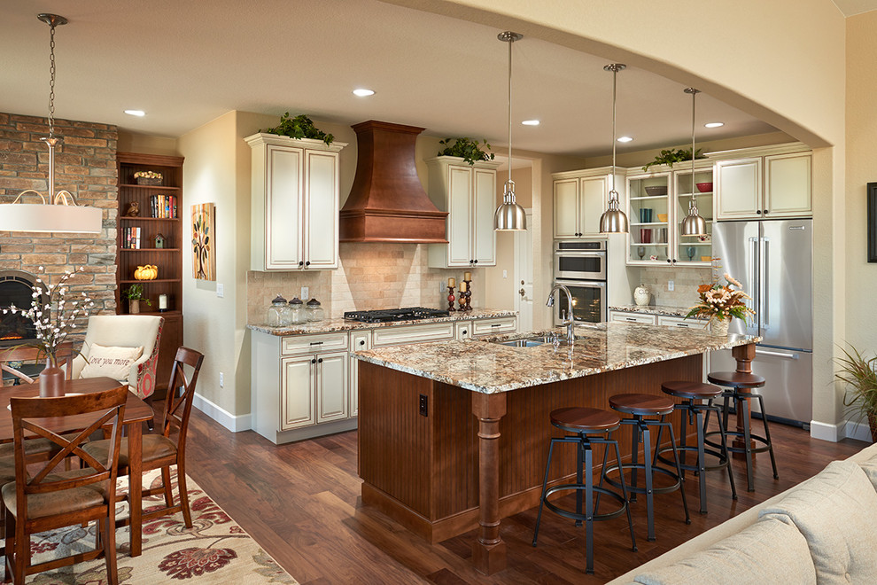This is an example of a country l-shaped open plan kitchen in Denver with a double-bowl sink, raised-panel cabinets, beige cabinets, beige splashback, stainless steel appliances, dark hardwood floors, with island, brown floor and brown benchtop.