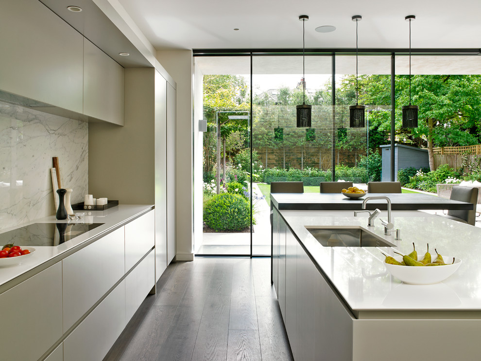 Contemporary galley open plan kitchen in London with an undermount sink, flat-panel cabinets, beige cabinets, white splashback, dark hardwood floors and with island.