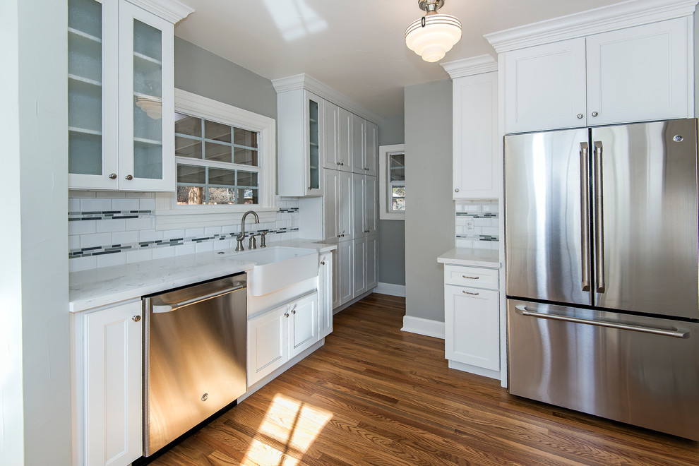 Example of a mid-sized transitional medium tone wood floor enclosed kitchen design with a farmhouse sink, recessed-panel cabinets, white cabinets, granite countertops, white backsplash, subway tile backsplash, stainless steel appliances and no island