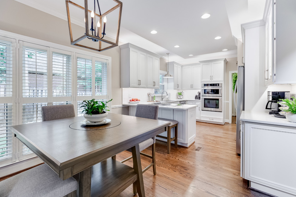 Mid-sized transitional u-shaped medium tone wood floor and brown floor eat-in kitchen photo in Birmingham with a double-bowl sink, recessed-panel cabinets, white cabinets, quartz countertops, white backsplash, subway tile backsplash, stainless steel appliances, a peninsula and white countertops