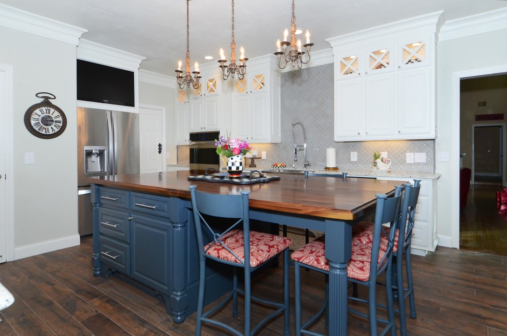 Photo of a mid-sized traditional u-shaped eat-in kitchen in Dallas with a farmhouse sink, raised-panel cabinets, blue cabinets, wood benchtops, grey splashback, mosaic tile splashback, stainless steel appliances, dark hardwood floors and with island.
