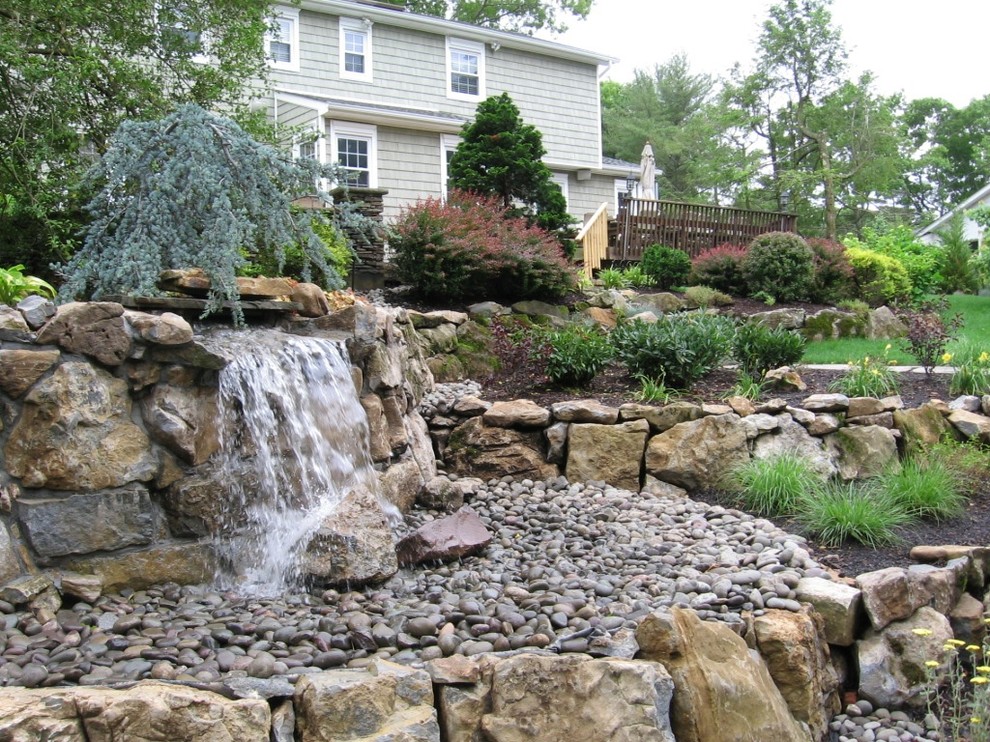 Photo of a tropical sloped garden in New York with with pond and natural stone pavers.