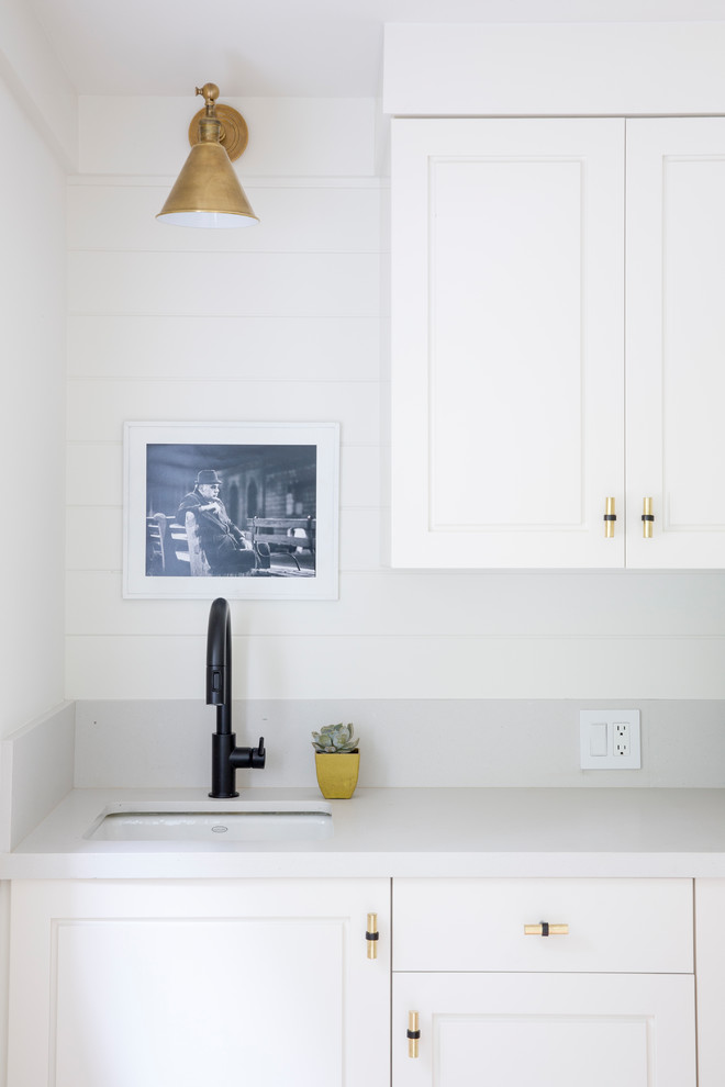Inspiration for a country l-shaped dedicated laundry room in San Francisco with an undermount sink, flat-panel cabinets, white cabinets, quartz benchtops, white walls, light hardwood floors, a side-by-side washer and dryer and grey benchtop.