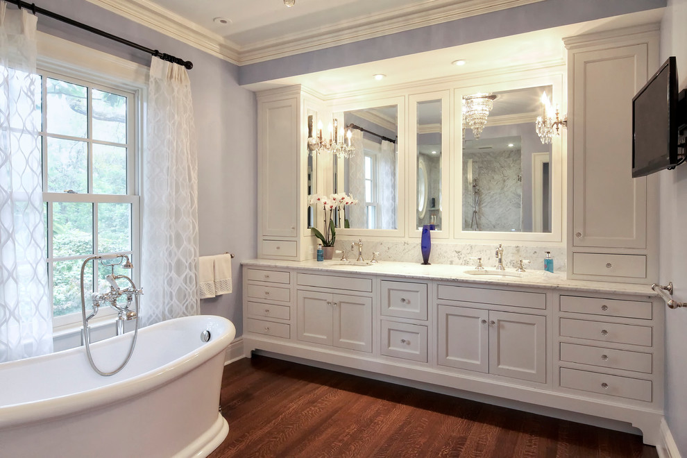 This is an example of a traditional master bathroom in New York with beaded inset cabinets, white cabinets, a freestanding tub, an alcove shower, white tile, marble, purple walls, medium hardwood floors, an undermount sink, marble benchtops, an open shower and white benchtops.