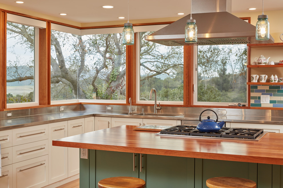 Photo of a large scandinavian u-shaped eat-in kitchen in San Luis Obispo with an integrated sink, white cabinets, stainless steel benchtops, multi-coloured splashback, ceramic splashback, stainless steel appliances, light hardwood floors, beige floor, raised-panel cabinets and with island.