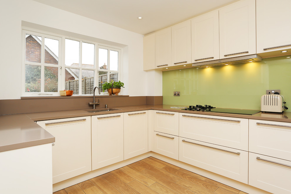 Design ideas for a mid-sized modern u-shaped kitchen in London with a single-bowl sink, beige cabinets, quartzite benchtops, green splashback, glass sheet splashback, black appliances and no island.