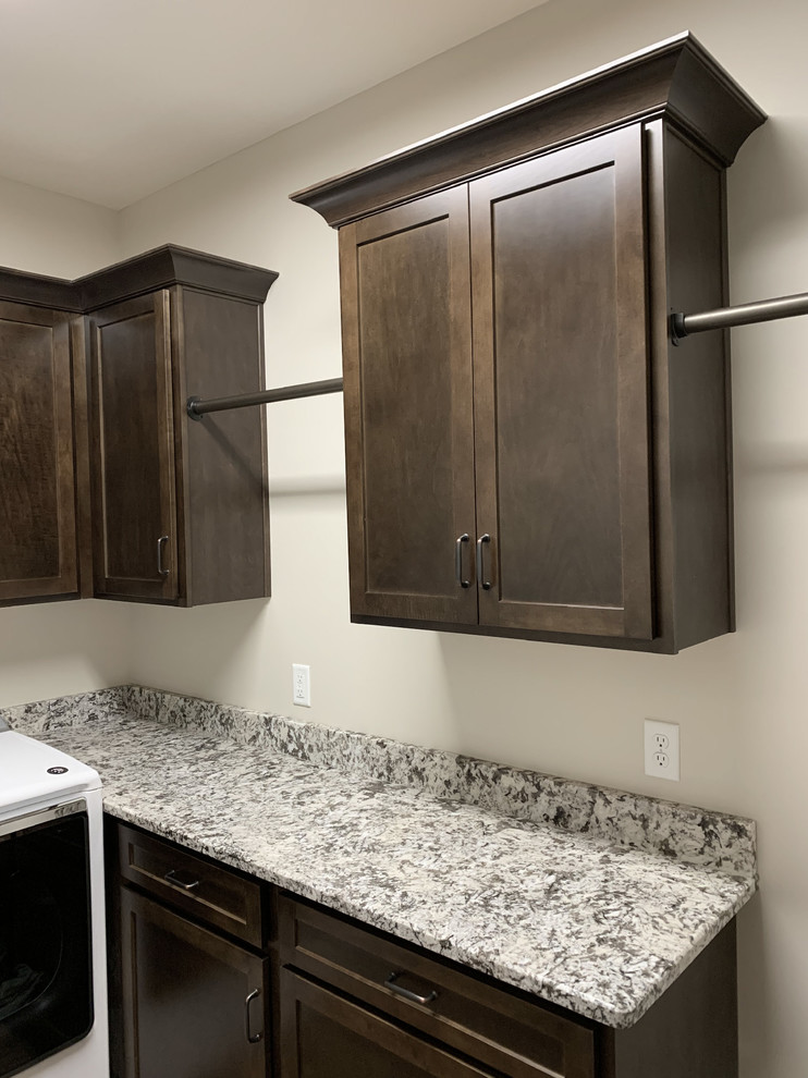 Photo of a transitional l-shaped dedicated laundry room in Other with shaker cabinets, dark wood cabinets, granite benchtops, beige walls, laminate floors, a side-by-side washer and dryer, beige floor and multi-coloured benchtop.