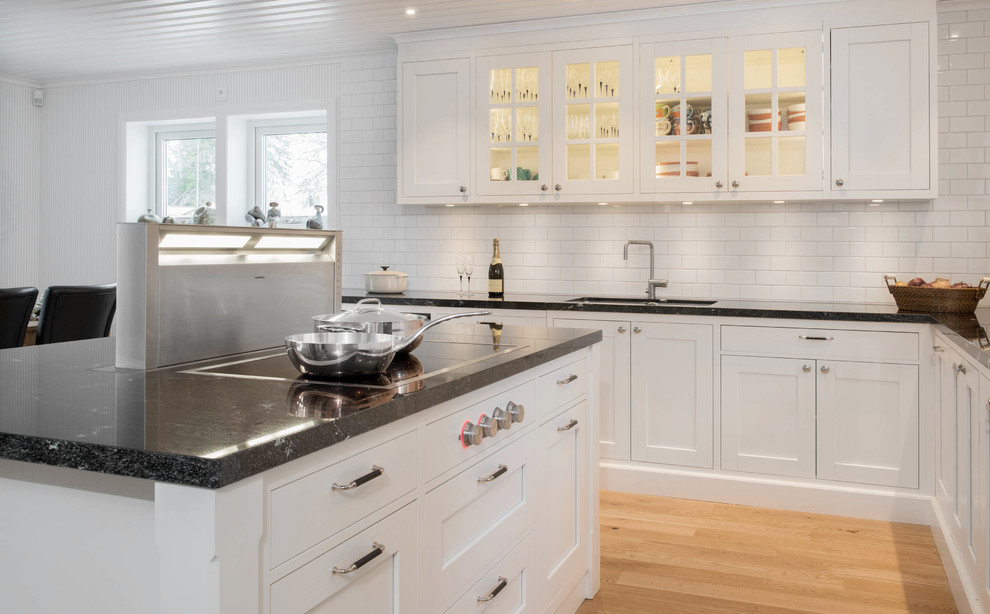 Traditional l-shaped eat-in kitchen in Stockholm with an undermount sink, shaker cabinets, white cabinets, granite benchtops, white splashback, porcelain splashback and stainless steel appliances.