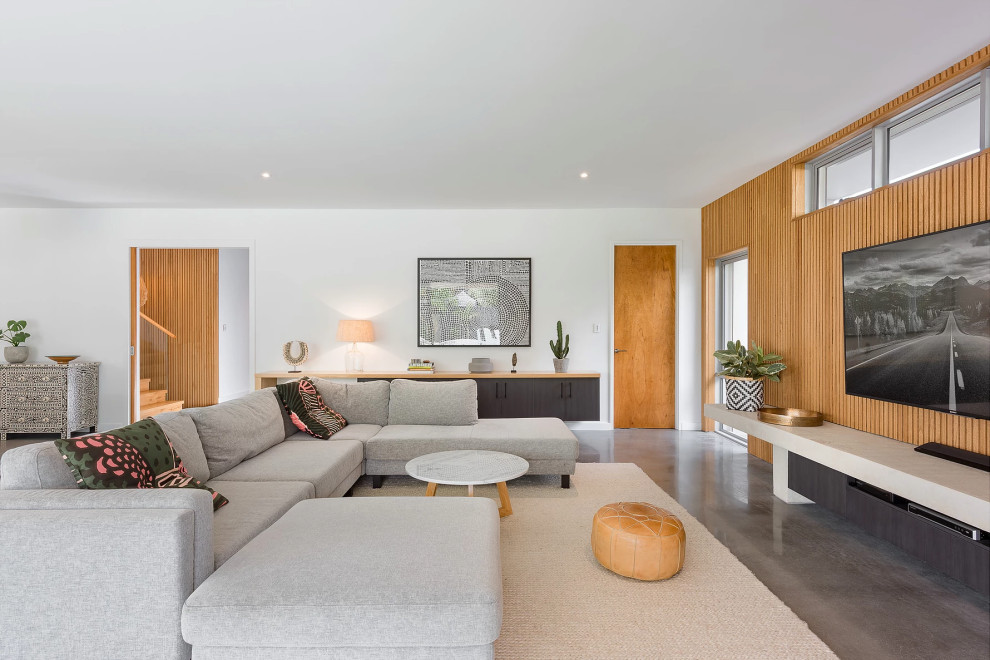 This is an example of a mid-sized contemporary open concept living room in Perth with concrete floors, no fireplace, a wall-mounted tv, grey floor and white walls.