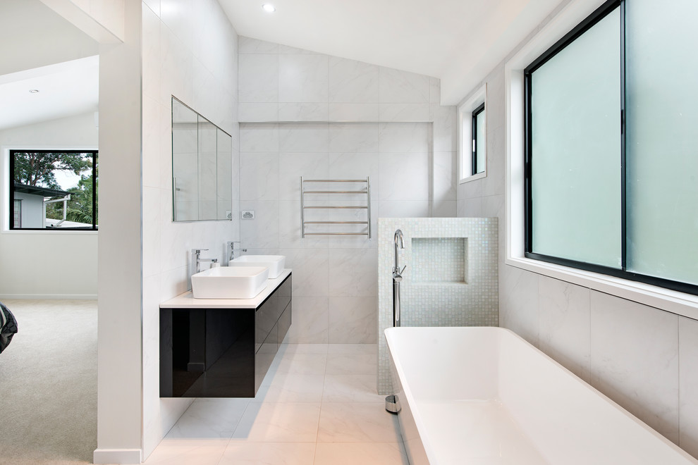 Inspiration for a contemporary bathroom in Brisbane with flat-panel cabinets, black cabinets, a freestanding tub, gray tile, a vessel sink, white floor and white benchtops.
