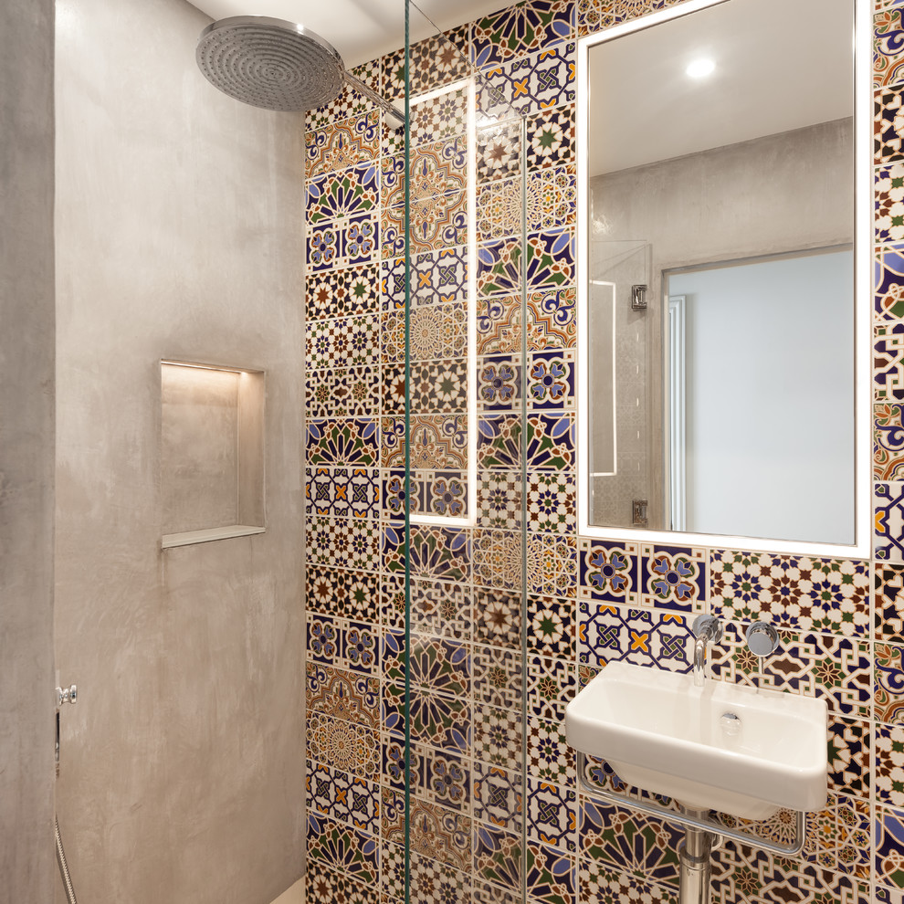 Mid-sized mediterranean 3/4 bathroom in London with an alcove shower, multi-coloured tile, grey walls, a vessel sink, a hinged shower door, flat-panel cabinets, brown cabinets, a drop-in tub, a one-piece toilet, glass sheet wall, light hardwood floors, wood benchtops and brown floor.