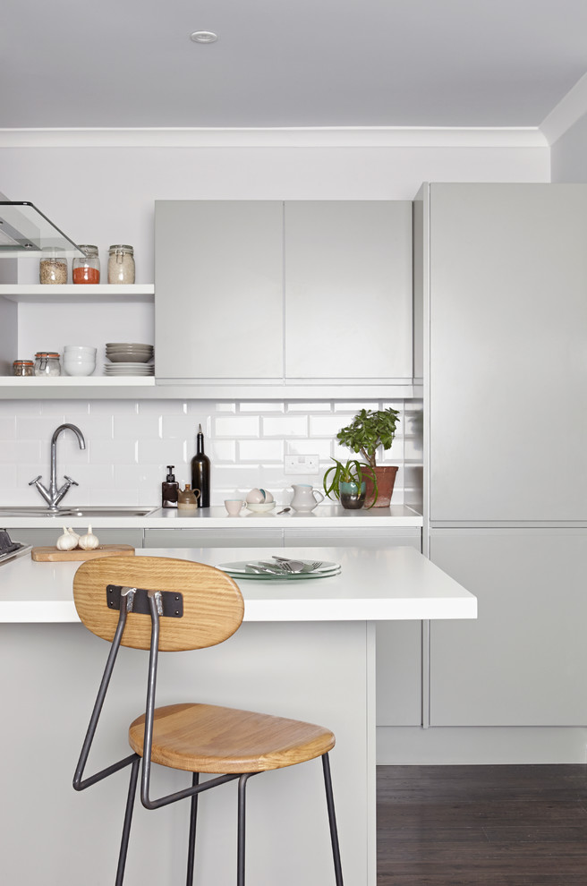 Photo of a contemporary kitchen in London with flat-panel cabinets, grey cabinets, laminate benchtops, white splashback, ceramic splashback, dark hardwood floors, with island and white benchtop.