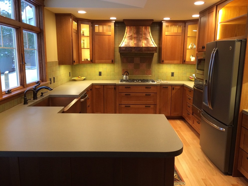 This is an example of an arts and crafts u-shaped eat-in kitchen in Grand Rapids with a farmhouse sink, concrete benchtops, green splashback and stainless steel appliances.